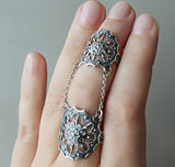 A hand showing a double ring with silver net of spider and goth herbal design.