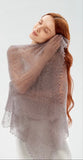 Close-up of a lightweight, knitted gray pashmina shawl with delicate lace edges wrapped around a woman's shoulders.