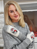 A pair of fluffy winter mittens in a two-tone grey and white pattern layout. The centerpiece shows a traditional winter themed illustration of a bird on a branch. Close-up view of a woman with premium 80 percent wool handwarmers designed specifically for severe cold weather conditions. The soft fabric blend provides dense insulation against freezing wind.
