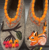  A pair of luxury gray wool felt slippers-chuni being showcased in a wooden surface. The artisan embroidery on the tops of the slippers shows an orange squirrel and a rowan berry palm, emphasizing the rare, collectible nature of hand-made footwear.