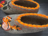 Close-up of handmade, exclusive gray valenki booties made of organic sheep wool, highlighting the natural, slightly textured finish of the premium felt and orange embroidery of a squirrel or a fox and a rowanberry palm on the top.