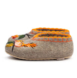 A top-down view of gray woolen house slippers featuring mismatched asymmetric designs inspired by forest nature. One slipper displays a detailed orange squirrel face with big eyes and a black outline, while the other slipper displays a beautiful botanical pattern of red viburnum or rowan berries hanging from a dark branch with green leaves. Both slippers are finished with a decorative orange embroidered border around the ankle opening.