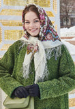 A Slavic woman wearing a green coat and floral white fringed headscarf in a snowy outdoor setting.