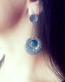 Close-up of a silver Armenian traditional earring with a blue gemstone worn by a person.