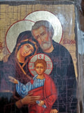 A religious icon painting of Saint Joseph, Mary, and the Infant Jesus, shown wrapped in protective plastic. The orthodox icon features gold halos, dark robes, and red and blue garments on a textured beige background.