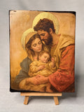 Handcrafted Holy Family wooden icon featuring Saint Joseph Mary and baby Jesus with gold leaf halos. Premium Catholic family blessing religious gift icon resting on a miniature wooden stand.