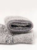 A close-up of a folded gray knit textile, likely mittens, showing a soft fuzzy texture and a subtle dark gray geometric pattern on a white background.