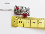 Decorative pendant with red stones and intricate design, measured against a ruler.