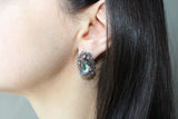 Close-up of a person wearing a decorative earring with a green pearly nacreous faceted gemstone.