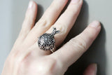 Hand wearing a decorative Armenian pomegranate ring on a neutral background
