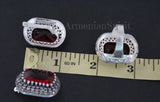 Silver earrings with red gemstones on a black background with a ruler for scale.