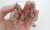 Silver hoop earrings with intricate small bell and Indian lotus flower designs held in a hand against a white background.