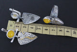 Silver jewelry pieces with yellow stones on a ruler for scale against a dark background