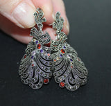 Ornate silver marcasite earrings with gemstones in feather shape held against a dark background
