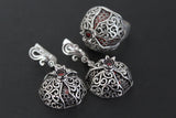 A picture showing a jewelry set consisting of a ring and earrings in pomegranate shape with traditional Armenian patterns and dark garnet gemstones on a black surface.