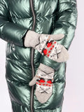 A close-up of a person wearing a shiny metallic green puffer jacket and gray knit mittens with red and black Nordic-style patterns. Soft and fluffy winter mittens crafted with a blend of 80 percent natural wool and 20 percent durable polyester material. The symmetric bird pattern creates a charming, timeless look perfect for outdoor cold-weather activities.