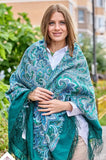 Woman wearing a green and blue patterned merino wool blanket shawl outdoors