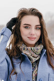 Woman wearing a blue coat and purple patterned patterned scarf in a snowy background