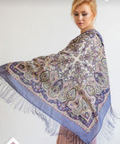 Woman wearing a large lavender patterned purple scarf with fringes on a plain background