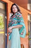 Woman wearing a floral green and pink woolen shawl and light blue dress standing in front of a building.