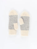 Two-tone white and grey winter mittens showcased against a shiny green puffer coat background. The detailed geometric knit pattern adds a timeless, elegant touch to seasonal cold-weather outerwear.
