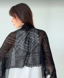 A very thin, lightweight black pashmina goat wool shawl laid on a woman`s shoulders from back, highlighting its delicate handwoven lace pattern and narrow rectangular shape.