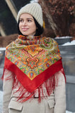 Person wearing a colorful patterned orange red merino wool scarf and beige knit hat outdoors.
