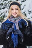 Woman wearing a blue woolen fringed scarf and dark coat in a snowy landscape
