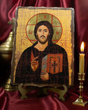 A religious Orthodox icon of Jesus Christ on a textured wooden plaque, displayed on a small stand between a brass censer and a lit candle on a dark red satin background. Handcrafted Christ Pantocrator wooden icon displayed on a wooden stand next to a lit candle and traditional brass censer. The Orthodox icon features a glossy varnished finish and vibrant gold halos.