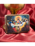 A rectangular religious icon plaque depicting the Last Supper, styled on a red satin fabric background with a gold chalice in the background.