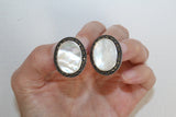 Oval earrings with marcasite and flat shell gemstones in a hand.