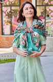 Woman in a green woolen shawl on her shoulders with pink vintage peony flowers standing on a paved path.
