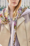 Close-up of a person wearing a decorative merino wool scarf with a beige coat against an urban background