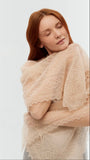 A person styling a narrow beige knitted pashmina wrap as an elegant headscarf, demonstrating its soft drape and classic neutral tone.