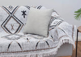 Decorative throw blanket with geometric patterns draped over a sofa with a pillow.