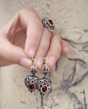 A photo showing a pair of oxidized silver pomegranate earrings which are holding by women`s fingers and a pomegranate ring on a middle finger.
