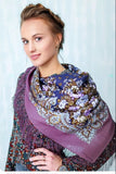 Woman wearing a patterned merino wool purple scarf with fringes against a light background