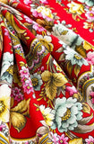 Close-up of colorful floral and paisley patterned red woolen shawl. A heavy-duty winter scarf swatch in vibrant red, decorated with large vintage-style flowers and detailed geometric paisley borders.