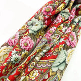Colorful woolen red shawl with floral and paisley patterns on a white background. A detailed close-up shot of a premium merino wool shawl fabric swatch. The material features a solid, vibrant red background heavily decorated with large vintage peony flowers in shades of soft pink and bright yellow, framed by complex multicolored paisley and scrollwork patterns.