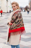 Woman wearing a patterned red woolen scarf with red trim on a city street.