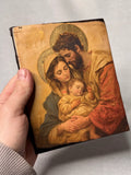 Catholic Holy Family religious icon on a solid wood block displayed on a small hand. Traditional style Holy Family art printed on wood with rustic edges and shimmering gold accents.
