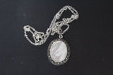 Vintage pendant with shell ivory gemstone and marcasite stones around the oval shape on a black surface.