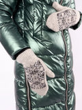 A close-up of a person wearing a shiny metallic green puffer jacket and light gray knit winter mittens with a gray and black snowflake pattern.