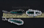 A pair of long silver earrings featuring marcasite and emerald green topaz, set against a dark background.

