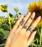 A person's hand showcasing three sterling silver Armenian taraz rings with blue enamel details, with sunflowers in the background.