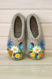 Pair of gray woolen chuni slippers with floral and butterfly designs on a wooden surface