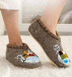 Brown woolen house boots-slippers with winter-themed designs on a white carpet