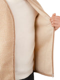 A close-up of a person wearing a beige sherpa-lined zip jacket over a cream ribbed sweater.