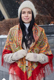 Woman wearing a colorful patterned orange red Slavic scarf with fringe on shoulders and white beanie in a snowy setting