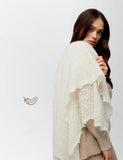 A detailed view of the warm ecru goat down woolen wrap on a woman`s shoulders. The tension reveals the knitted lace like patterns and lightweight elasticity of the gossamer fabric.